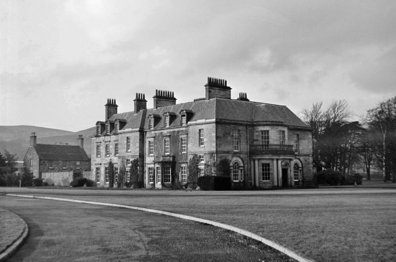 Easter Bush House on the Bush Estate near Edinburgh, a large stone country house with multiple chimneys and a wide lawn and curved driveway in front, hills visible in the background
